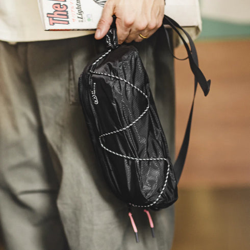 Person holding a black mesh bag with white stitching, blurred background